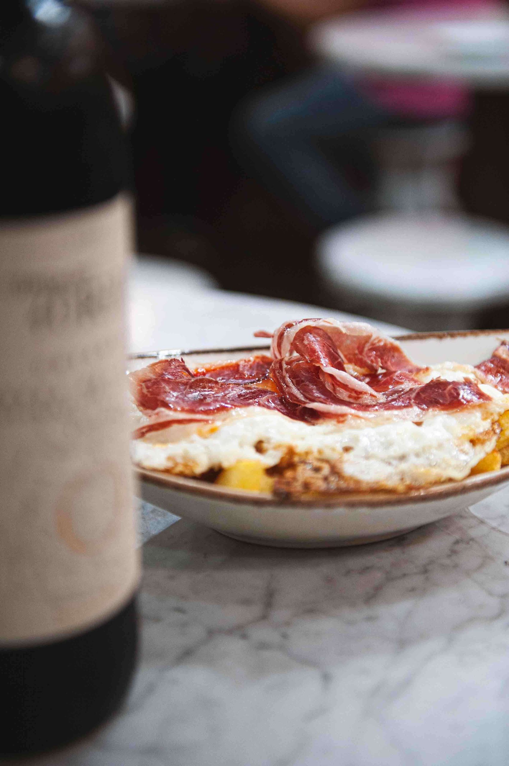 tapa de patatas con jamón y huevo y botella de vino lateral